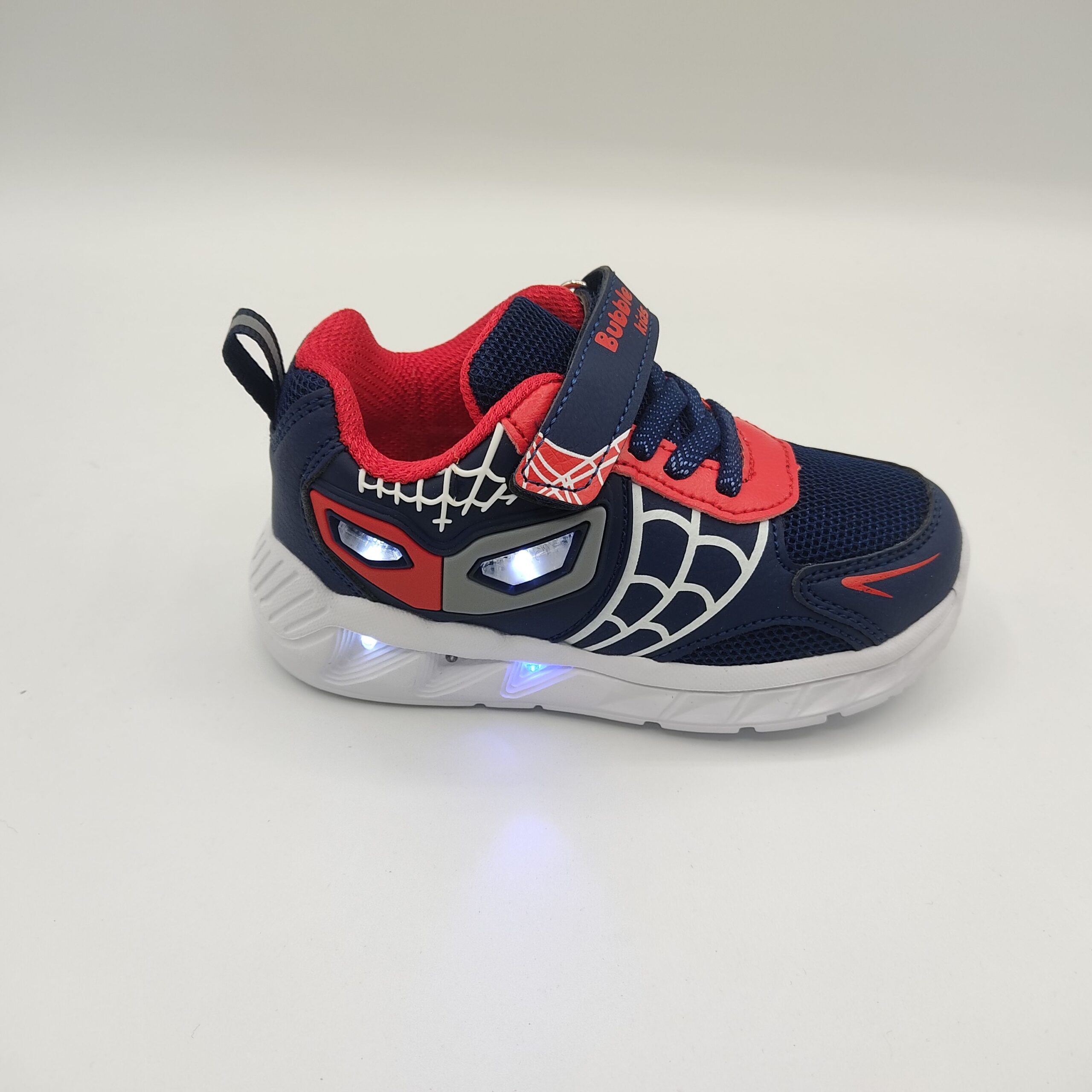 Zapatilla niño Bubble Kids C1277 Marino luces Zapatillas deportivas para niño de la marca Bubble Kids, modelo C1277 en color marino. Suela blanca de poco peso con luces. Fabricada en textil marino con detalles rojos simulando un antifaz con luces en la zona de los ojos y blancos simulando una telaraña. Cierre con cordón elástico y velcro en color marino y rojo.